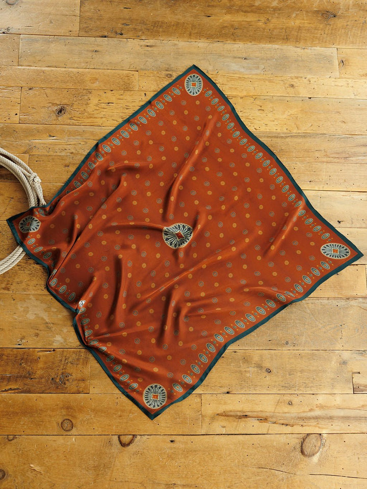 Rust-colored square San Miguel Silk Scarf featuring a pattern of small tan dots and a dark green border with decorative medallions, styled as a Southwest silk scarf.