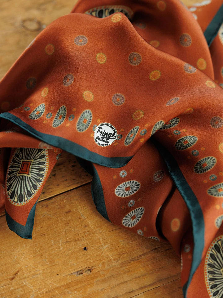 San Miguel Silk Scarf in rust-colored silk with a dark green border and a repeating pattern of small circular motifs.