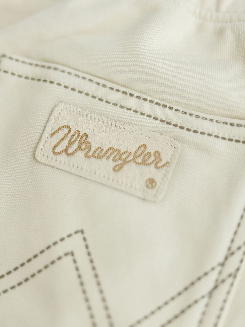 Close-up of a beige fabric label with "Wrangler" stitched in cursive, attached to the Sanger Natural Boot Stitch Set by Savannah Sevens western life{&}style, featuring visible brown stitching and relaxed fit pocket details.
