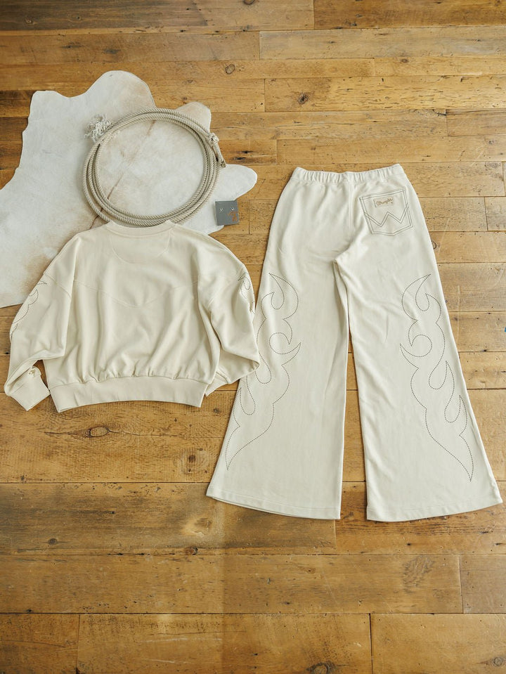 The Sanger Natural Boot Stitch Set from Savannah Sevens western life{&}style, featuring a cream-colored sweatshirt and matching high-waisted wide-leg pants, is displayed on a wooden floor beside a coiled rope and white animal hide rug.