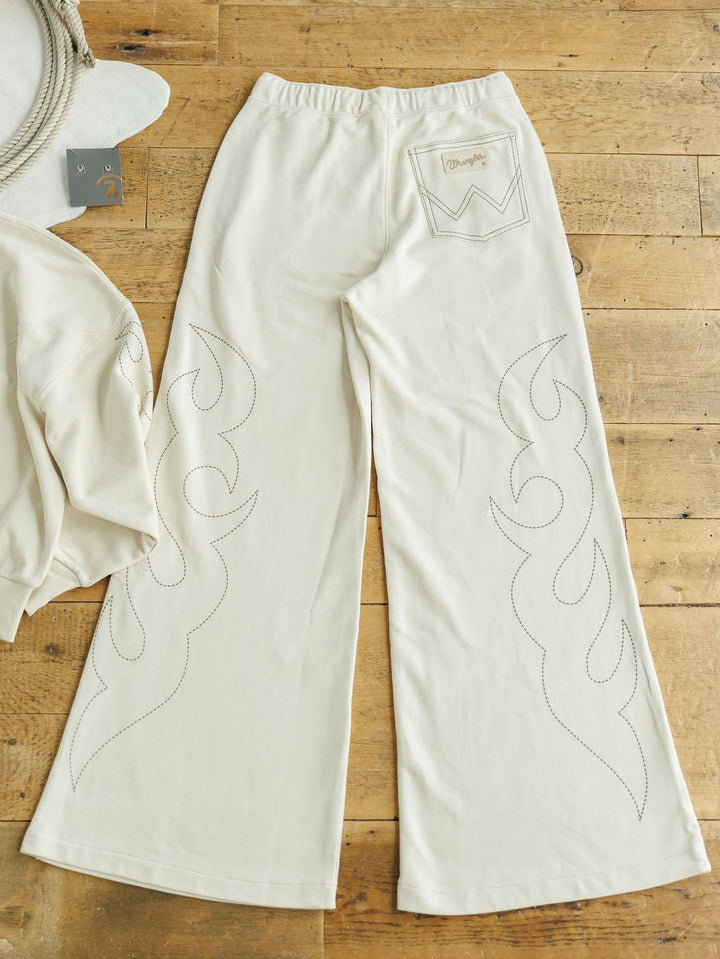The Sanger Natural Boot Stitch Set by Savannah Sevens western life{&}style features cream high-waisted, relaxed fit pants with flame-like stitching, laid flat on a wooden floor with the matching jacket partially visible to the left.