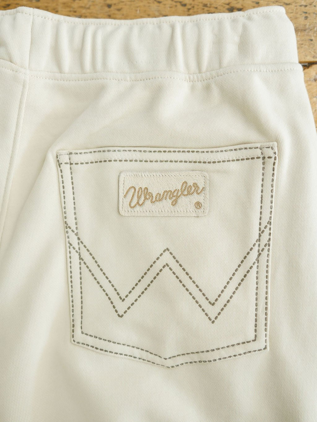 Close-up of a cream-colored pocket with brown stitching and a logo patch above a stitched W, from the Sanger Natural Boot Stitch Set by Savannah Sevens western life{&}style. This relaxed fit piece is crafted from denim or similar material.