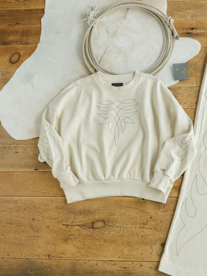 The Sanger Natural Boot Stitch Set by Savannah Sevens western life{&}style features a cream sweatshirt with abstract stitching, laid flat beside matching textile and relaxed fit, high-waisted pants with similar stitched designs.