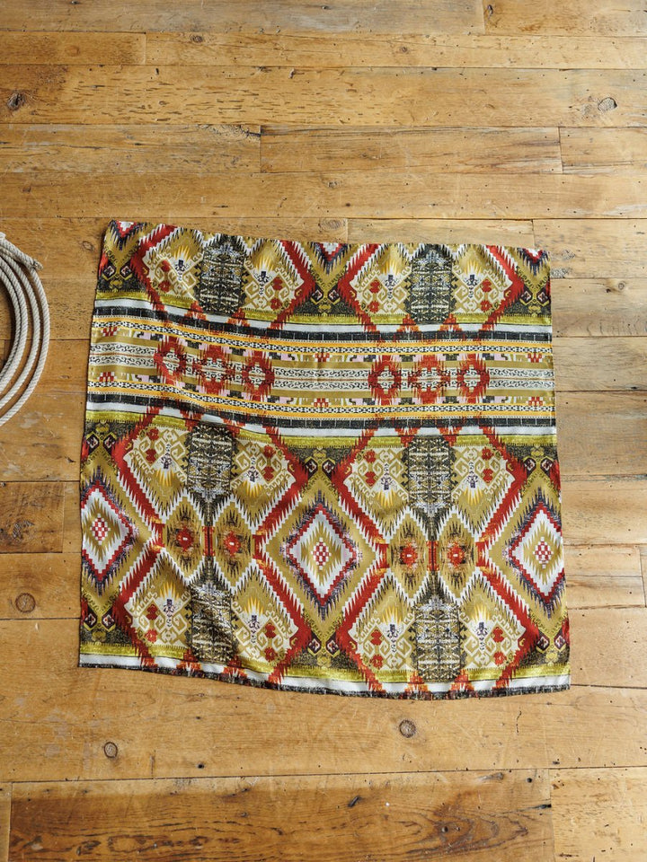 A rectangular rug with a vibrant red, yellow, and green geometric pattern covers the wooden floor. The Santa Fe Wild Rag by Savannah Sevens Western Chic is partially visible, coiled on the left side of the image.