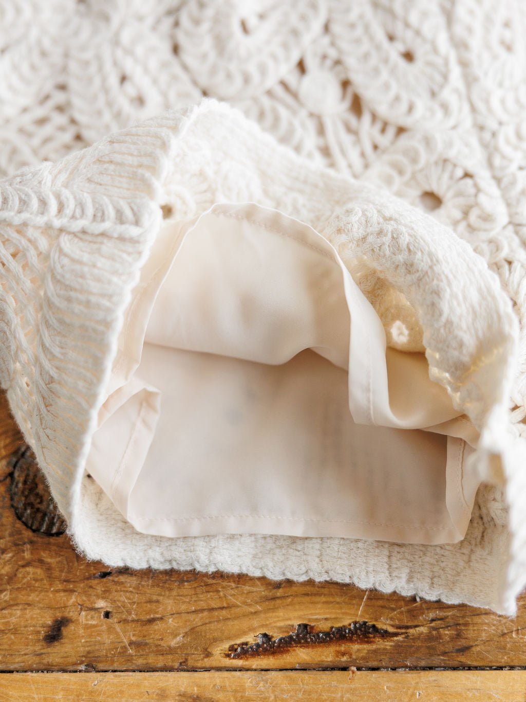 A close-up of The Saratoga by Savannah Sevens western life{&}style—a cream crocheted bag with a beige fabric lining, open to reveal the interior, resting on rustic wood; perfect for pairing with crochet or cream shorts.