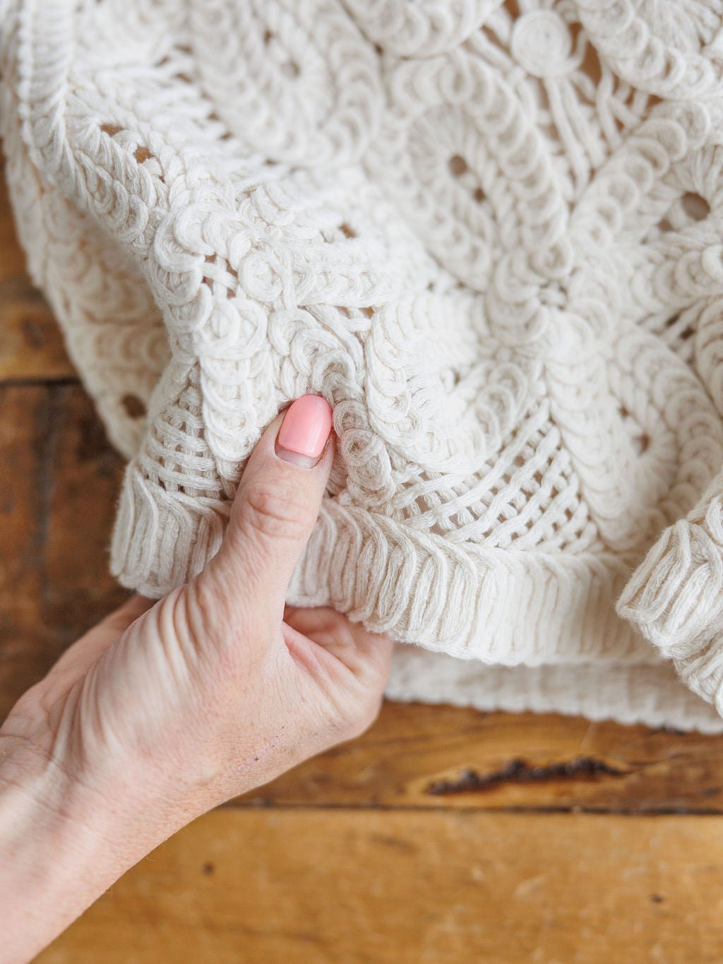 A hand holds the edge of The Saratoga cream crochet shorts by Savannah Sevens western life{&}style, highlighting their intricate design on a wooden surface.