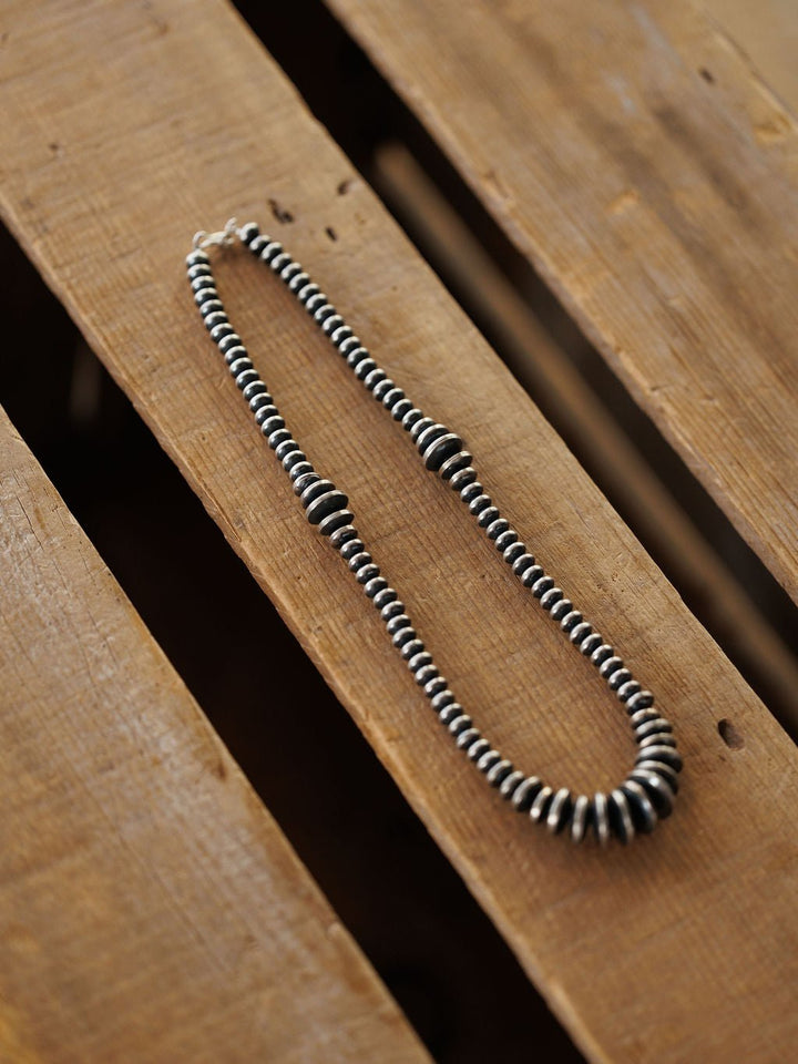 Sarita Graduated Navajo Pearl Necklace in sterling silver arranged in an oval shape on wooden planks.