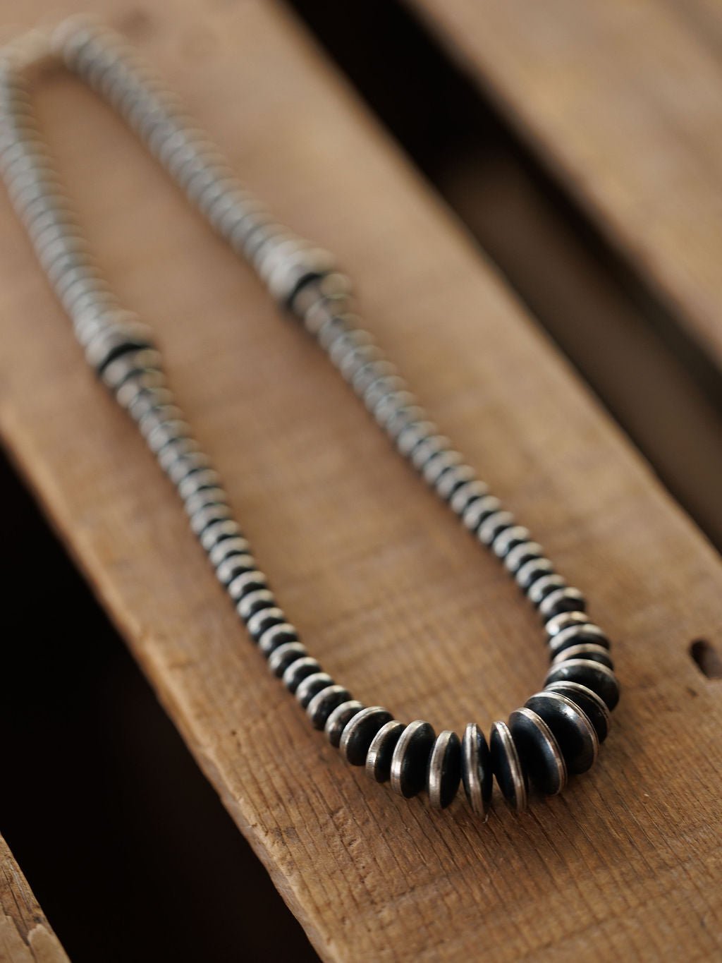 A Sarita Graduated Navajo Pearl Necklace made of sterling silver resting on a wooden surface.