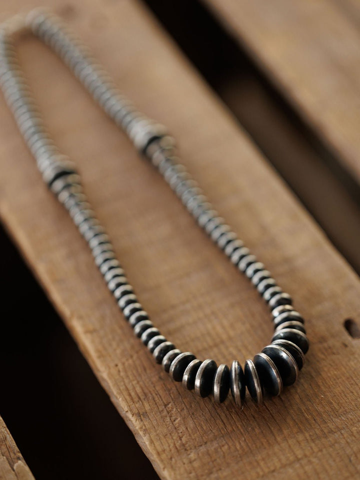 A Sarita Graduated Navajo Pearl Necklace made of sterling silver resting on a wooden surface.