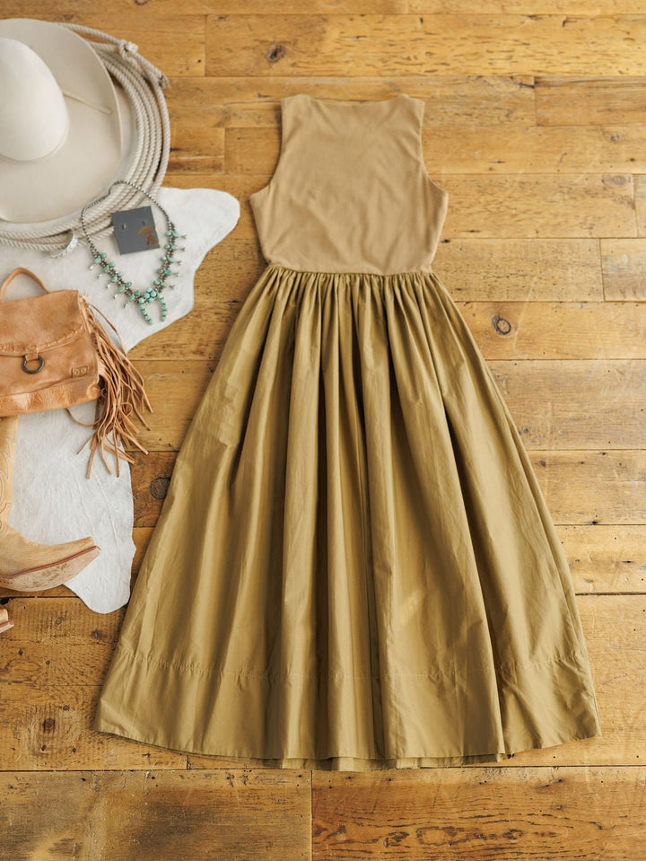 The Saville Bronze Dress by Savannah Sevens western life{&}style, a sleeveless cotton midi with fitted bodice and gathered skirt, is laid flat on wood next to a beige cowboy hat, boots, tan fringe bag, turquoise jewelry, and cowhide rug.