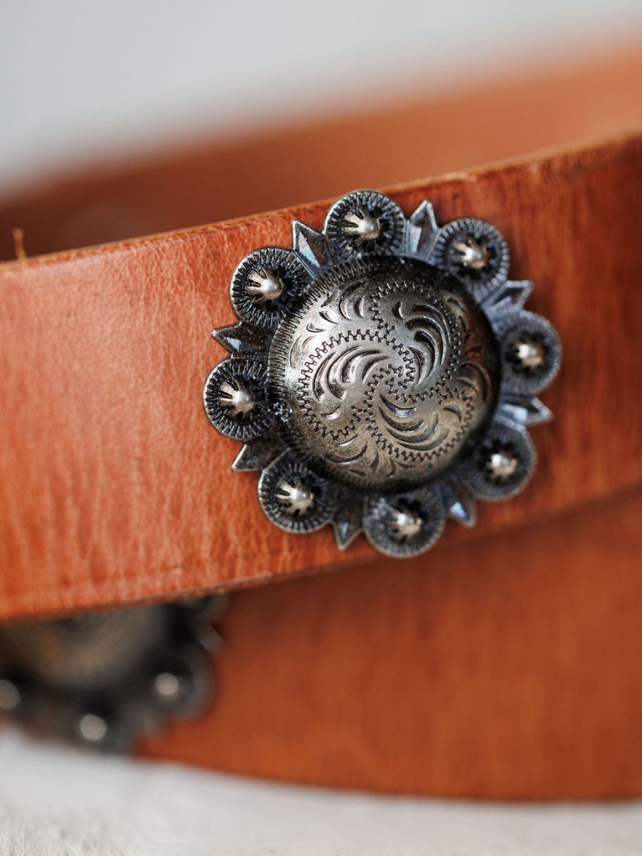 A close-up of the Sedona Belt by Savannah Sevens western life{&}style, showing its cognac leather and an ornate, circular southwest silver concho with intricate engraved designs and scalloped edges.