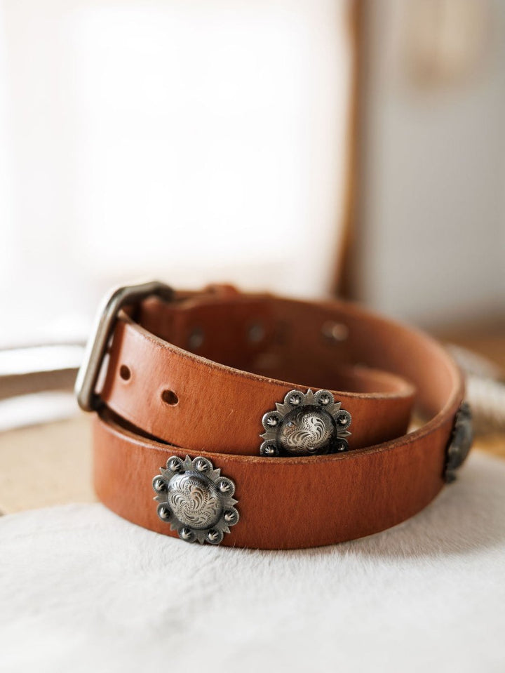 The Sedona Belt by Savannah Sevens western life{&}style, crafted in cognac leather with southwest silver conchos and a silver buckle, is coiled on a light surface in gentle light.
