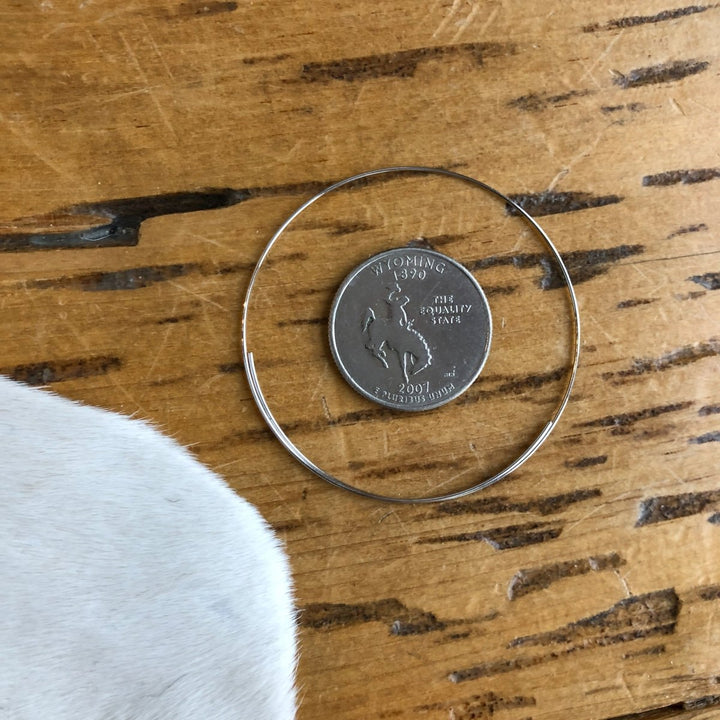 A Wyoming state quarter and a thin Seminole Earring by Savannah Sevens western life{&}style rest on a scratched wooden surface, with part of a white cowhide visible in the lower left corner.
