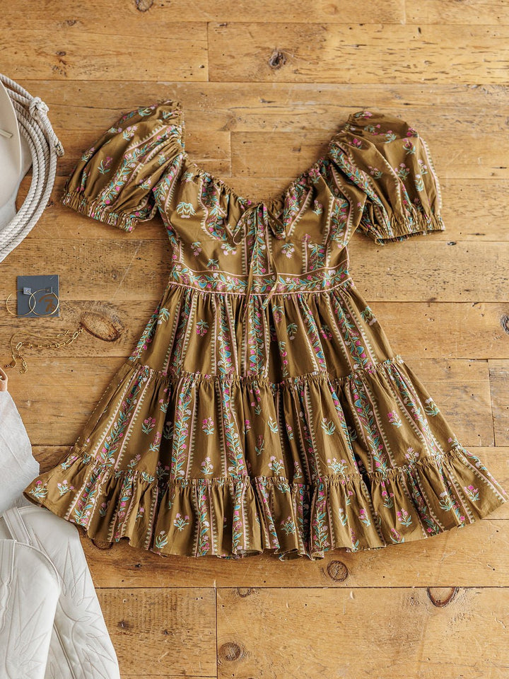 The Senoia Floral Puff Sleeve Dress by Savannah Sevens western life{&}style is laid flat on a wooden floor, styled with jewelry and a white bag partially visible.