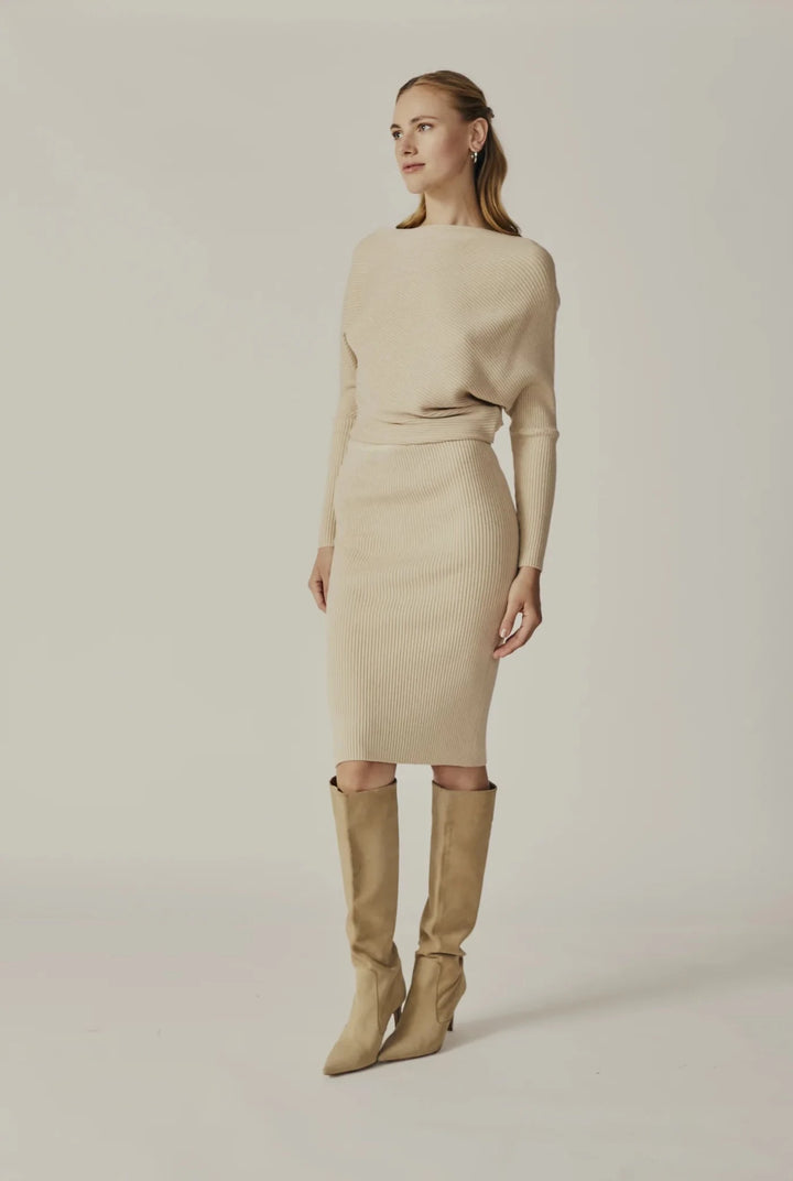 A woman wears the Shawnee Hills Oatmeal Ribbed Long Sleeve Dress by Savannah Sevens western life{&}style, paired with tan knee-high boots, standing against a plain light background.