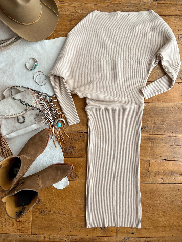 The Shawnee Hills Oatmeal Ribbed Long Sleeve Dress by Savannah Sevens western life{&}style is displayed on a wooden floor with brown suede boots, a tan hat, silver and turquoise jewelry, a fringe handbag, and a white textured cloth.