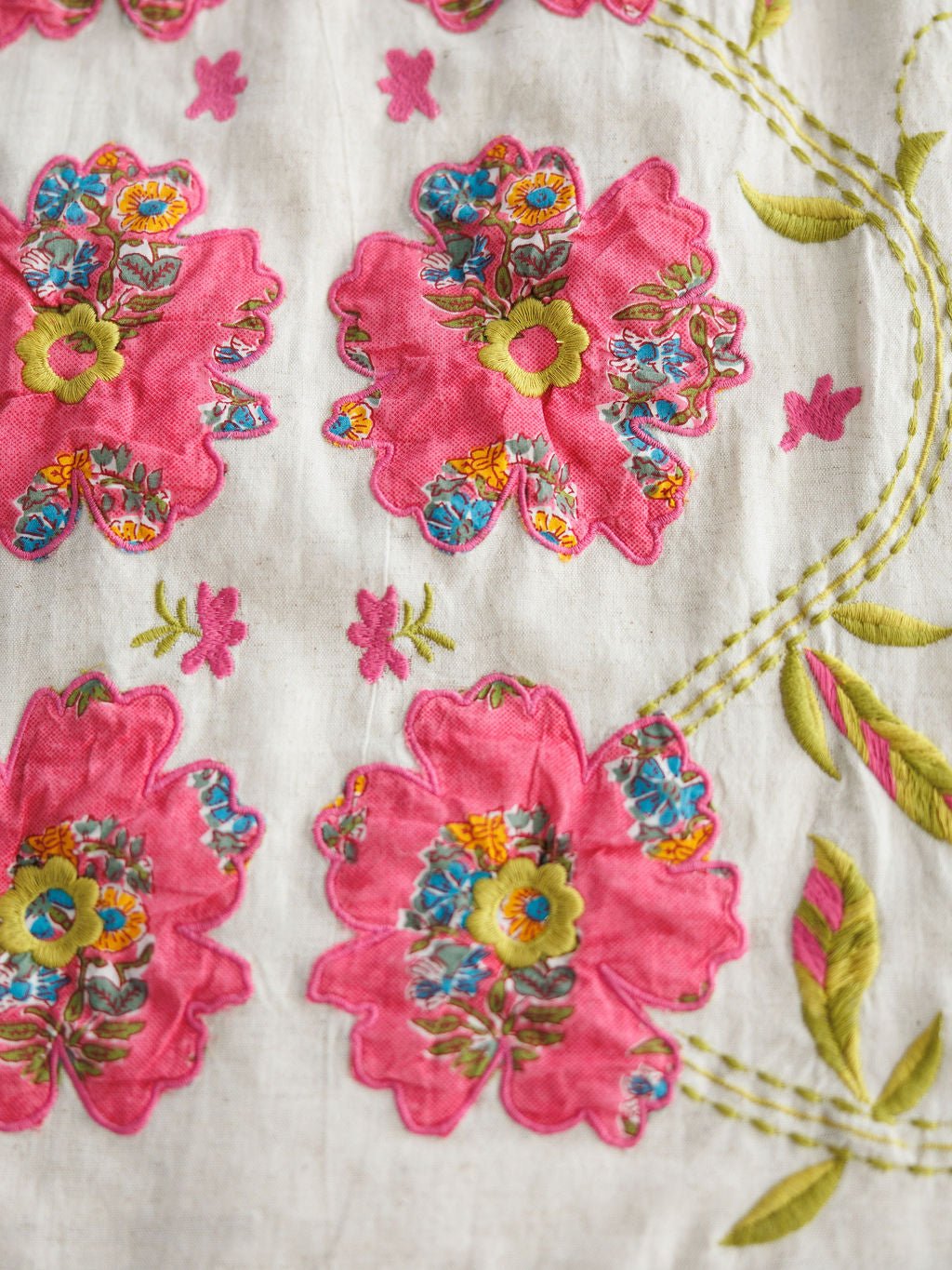 Close-up of the Sidell Floral Embroidered Dress by Savannah Sevens western life{&}style, showcasing large pink flowers with colorful patterns, green and yellow centers, and stitched green leaves on a white background.
