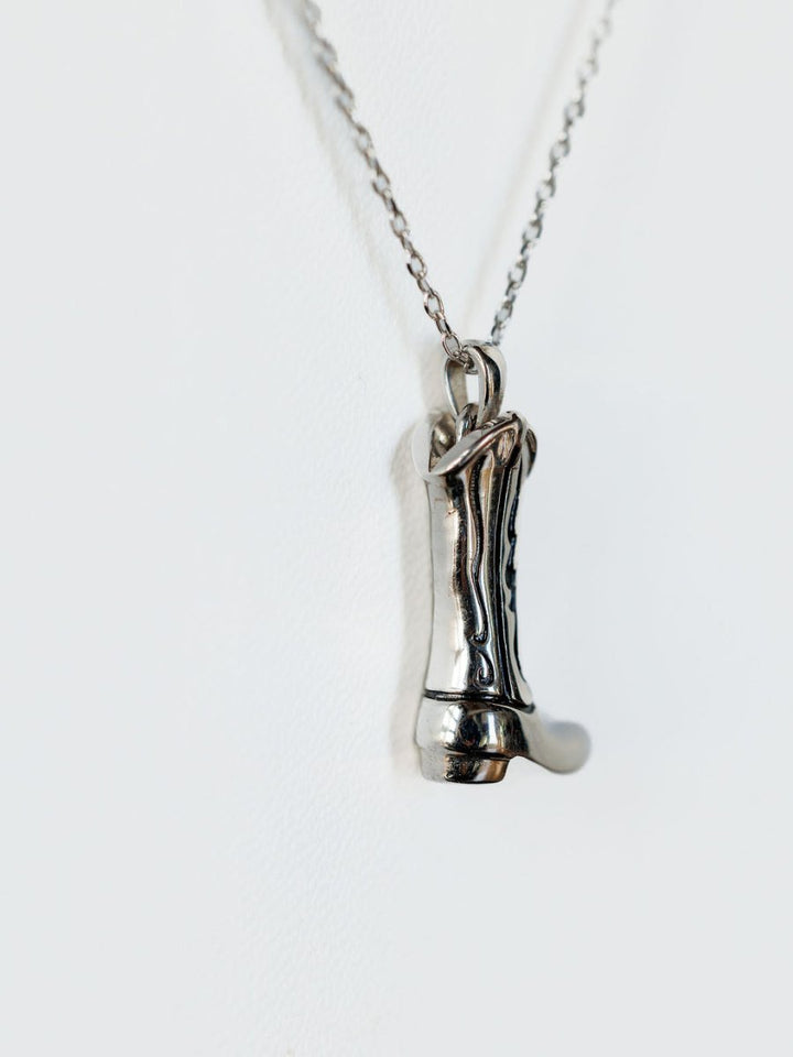 The Silver Cowgirl Boot Necklace by Savannah Sevens western life{&}style features a detailed boot pendant, bringing western charm against a plain white background.