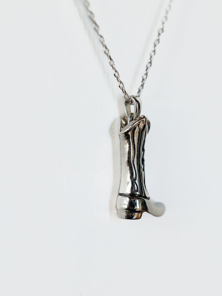 The Silver Cowgirl Boot Necklace by Savannah Sevens western life{&}style features a detailed boot pendant, bringing western charm against a plain white background.