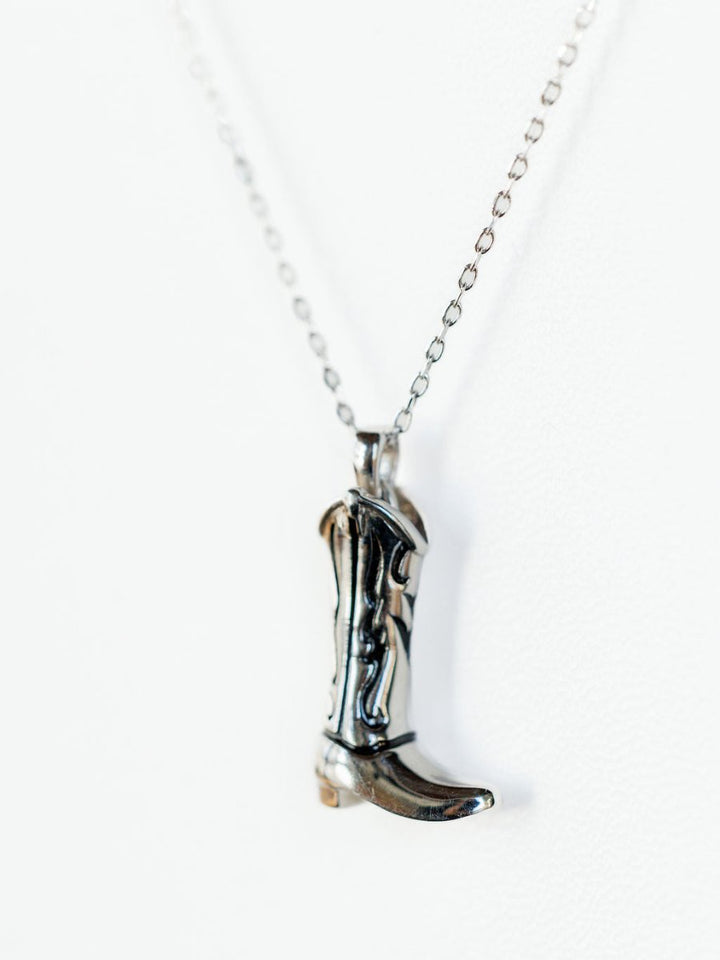 The Silver Cowgirl Boot Necklace by Savannah Sevens western life{&}style features a silver boot pendant on a delicate chain, shown against a white background.