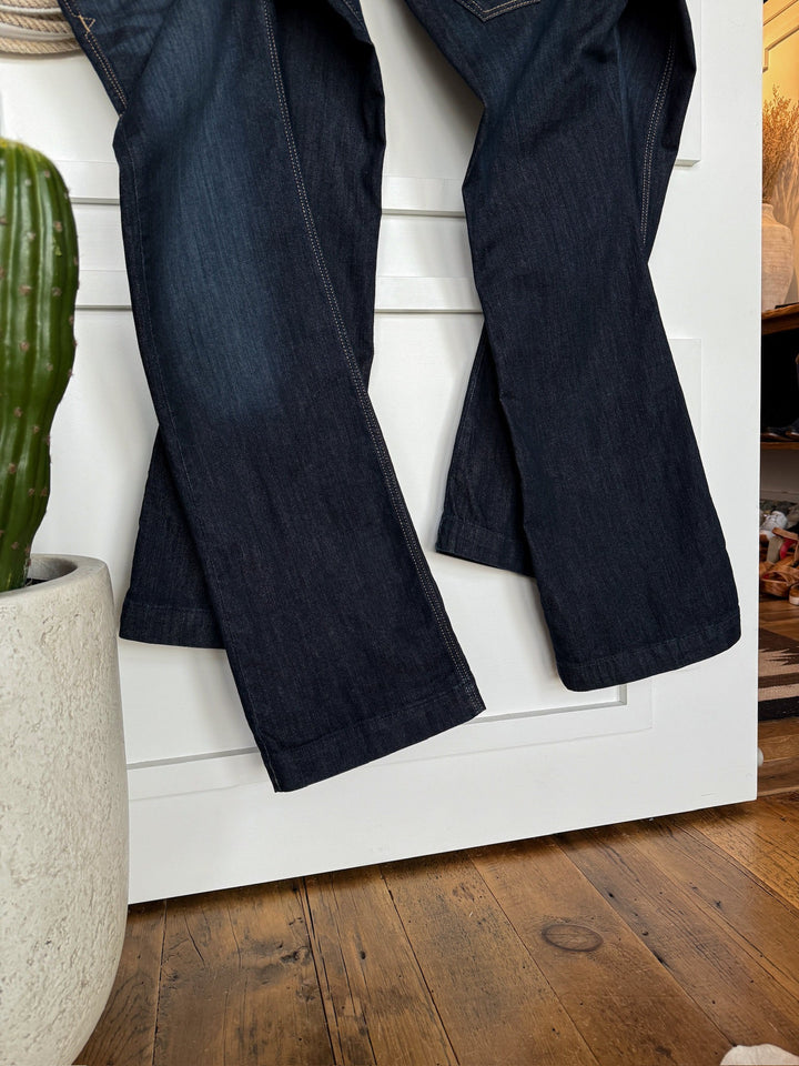 The Slade Perfect Rise Trouser Jean by Savannah Sevens western life{&}style hangs on a white door indoors, with a green cactus in a white pot placed on the wooden floor nearby.