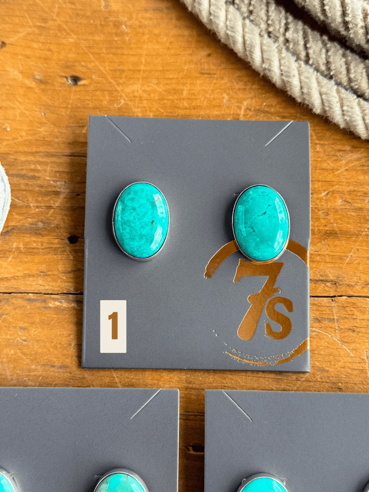 A pair of handmade Slidell Earrings by Savannah Sevens western life{&}style, shown on a gray card labeled "1," rest on a wooden surface with a thick, coiled rope in the background.