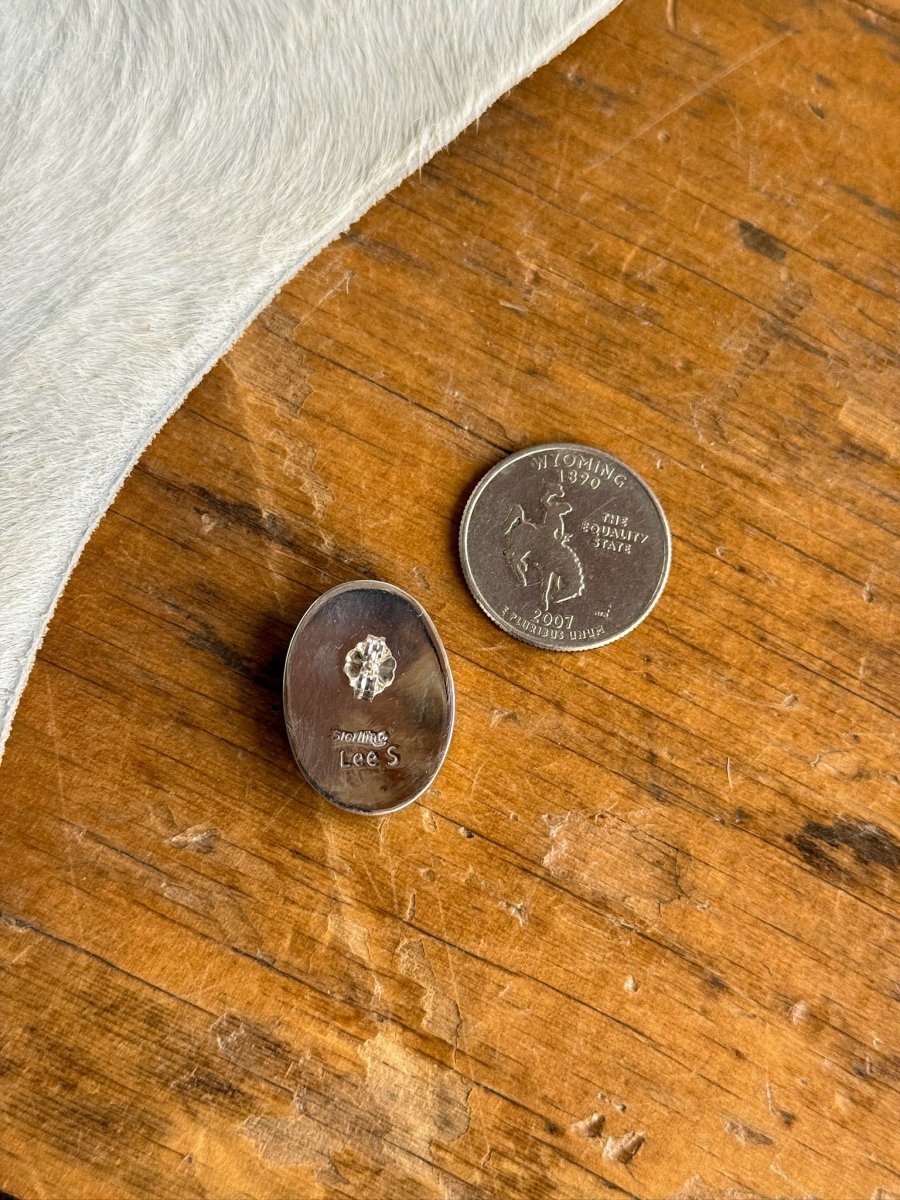 A pair of Slidell Earrings by Savannah Sevens western life{&}style rests beside a Wyoming state quarter on a wooden surface, with white animal hide visible in the corner.