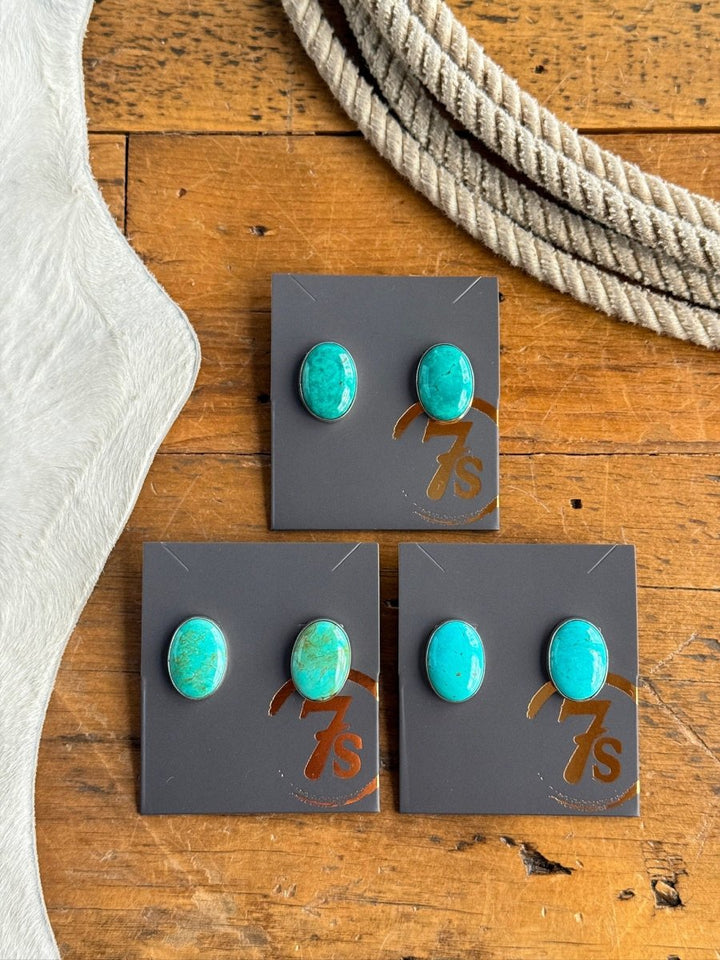 Three pairs of Slidell Earrings by Savannah Sevens western life{&}style are shown on black cards with a gold 7s logo, displayed on a wooden surface beside white cowhide and coiled rope.