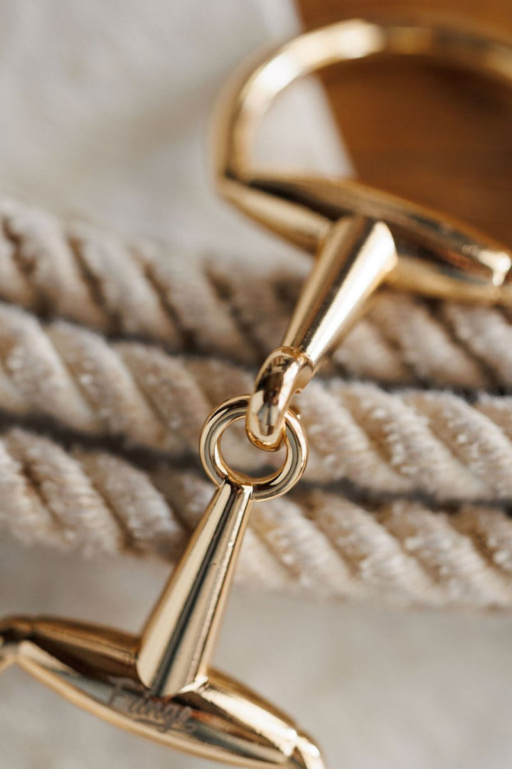 Close-up of the Savannah Sevens western life{&}style Snaffle Bit Scarf Buckle in gold, attached to a cream twisted rope, with a softly blurred background.