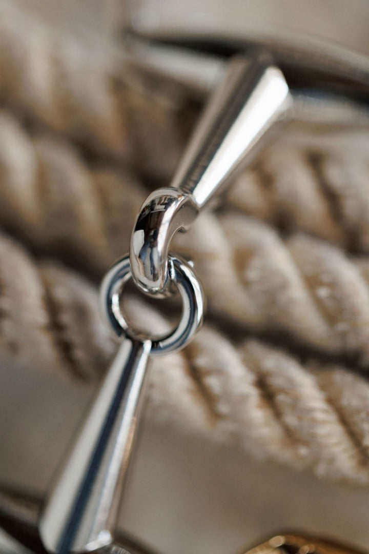 Close-up of the Savannah Sevens western life{&}style Snaffle Bit Scarf Buckle attached to a thick, twisted beige rope, showcasing its shiny metal finish and textured details.