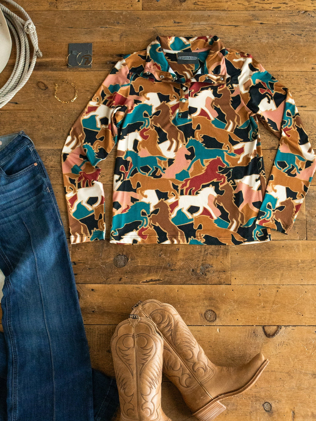 Socorro Western Graphic Top by Savannah Sevens western life{&}style, paired with blue jeans, tan cowboy boots, a bracelet, and silver earrings, arranged on a wooden floor.