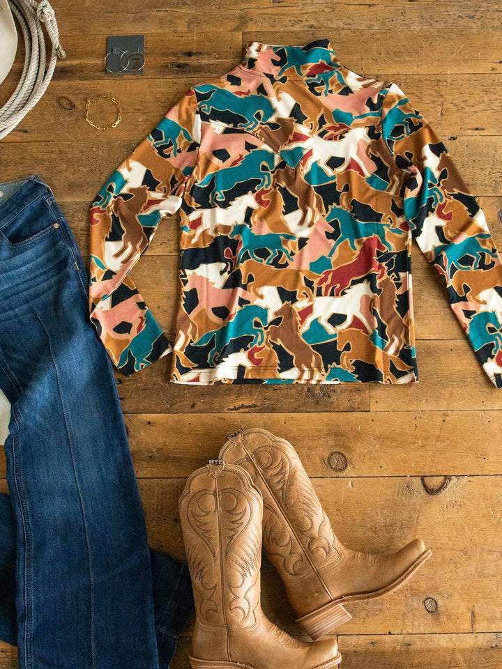 The Socorro Western Graphic Top from Savannah Sevens western life{&}style, blue jeans, tan cowboy boots, jewelry, and a rope are arranged in a flat lay on a wooden floor.