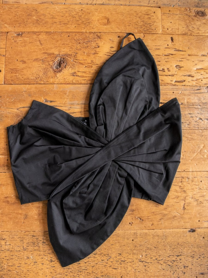 The Solvay top by Savannah Sevens western life{&}style features a black, strapless twisted knot crop top, shown laid flat on a wooden floor—ideal for pairing with high-waisted pants.