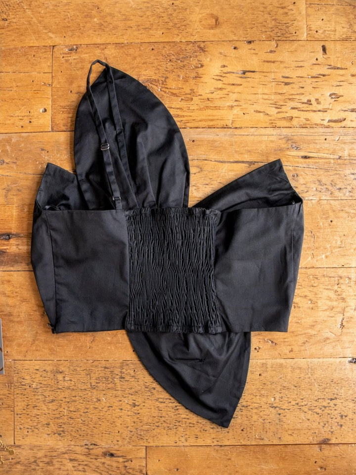 The Solvay {Set} by Savannah Sevens western life{&}style features a black crop top and pants with a ruched elastic panel, long fabric pieces, and a strap, displayed flat on a wooden surface.