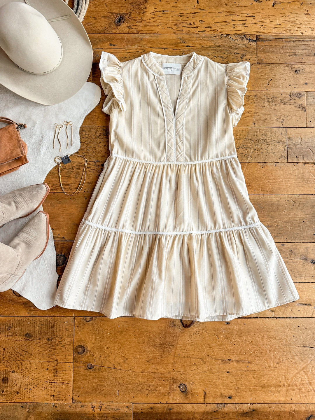 The Somerton Oatmeal Striped Dress by Savannah Sevens western life{&}style is styled flat with a beige hat, tan boots, a brown bag, and gold hoop earrings for an effortlessly chic earth tone look.