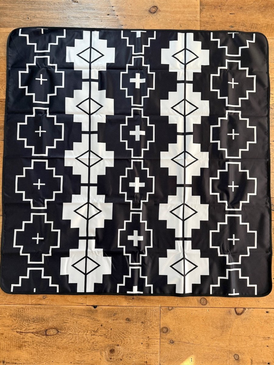 The Southwest Splat Mat from Savannah Sevens western life{&}style features a black and white symmetrical geometric pattern with squares, diamonds, and crosses. It has a nonslip backing for secure placement on wooden floors.
