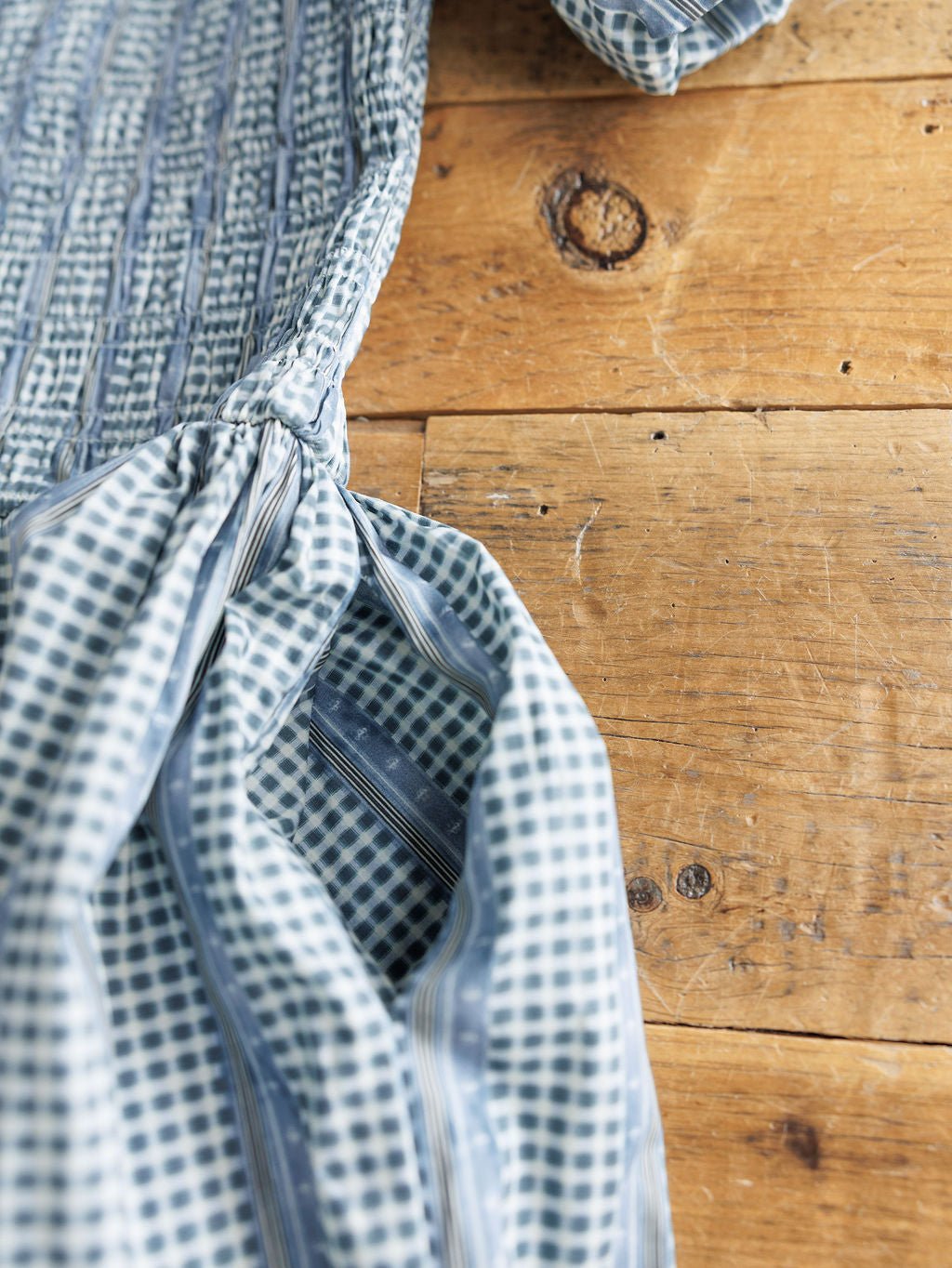The Springfield Blue Cotton Puff Sleeve Dress by Savannah Sevens western life{&}style features a blue and white checkered pattern with gathered stitching, shown on a rustic wooden surface with natural knots and grain.