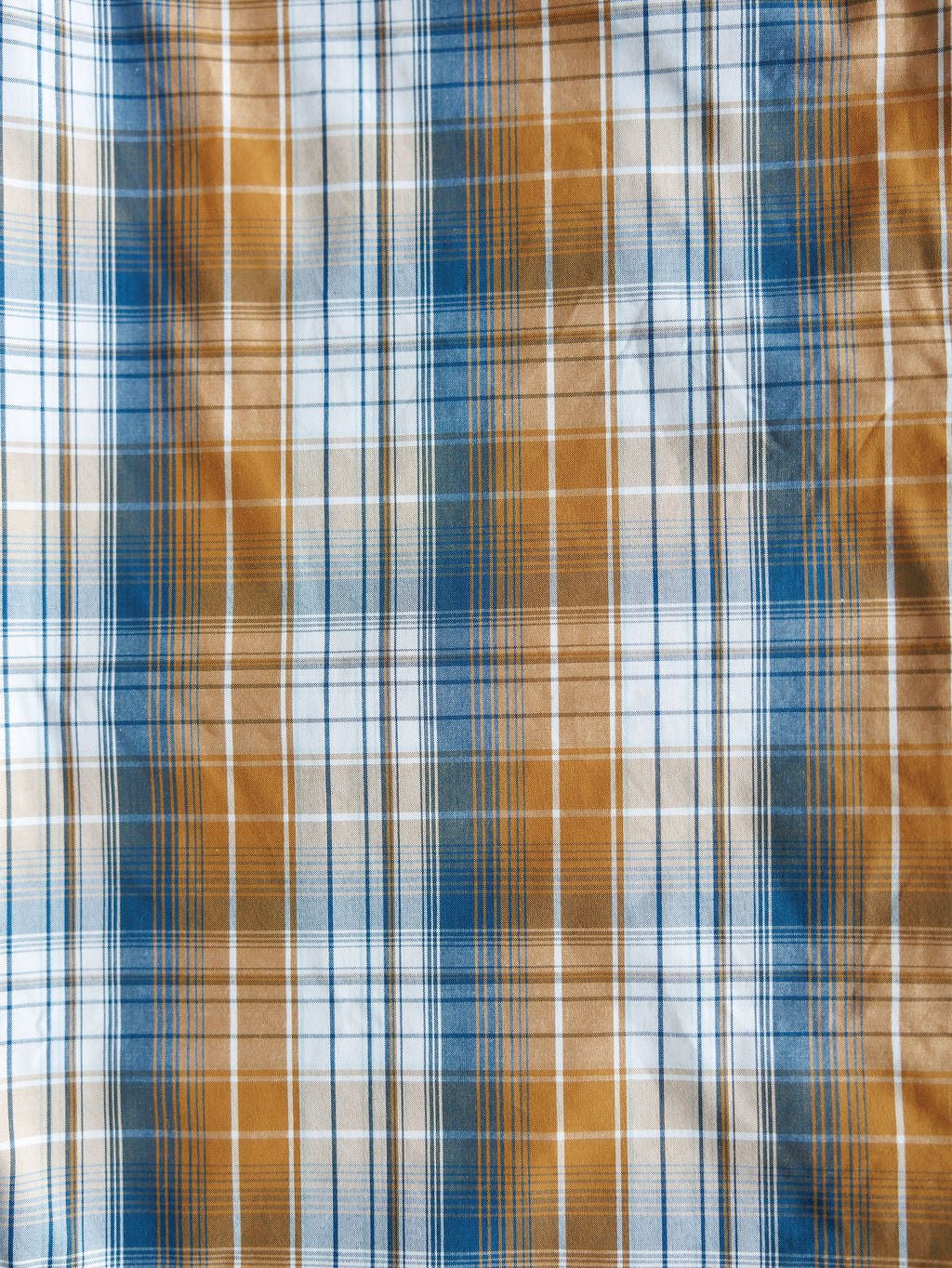 A close-up of the Stapleton Ariat Men's Plaid Pearl Snap by Savannah Sevens western life{&}style shows intersecting blue, white, and brown lines forming a grid pattern on the men's long sleeve shirt. The fabric's texture is clearly visible.