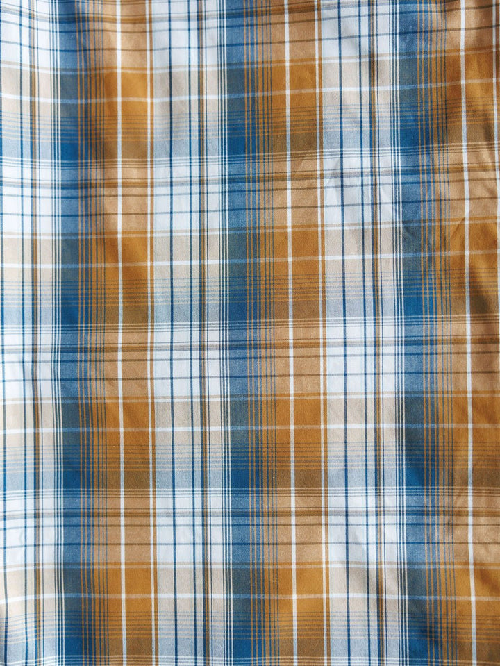 A close-up of the Stapleton Ariat Men's Plaid Pearl Snap by Savannah Sevens western life{&}style shows intersecting blue, white, and brown lines forming a grid pattern on the men's long sleeve shirt. The fabric's texture is clearly visible.