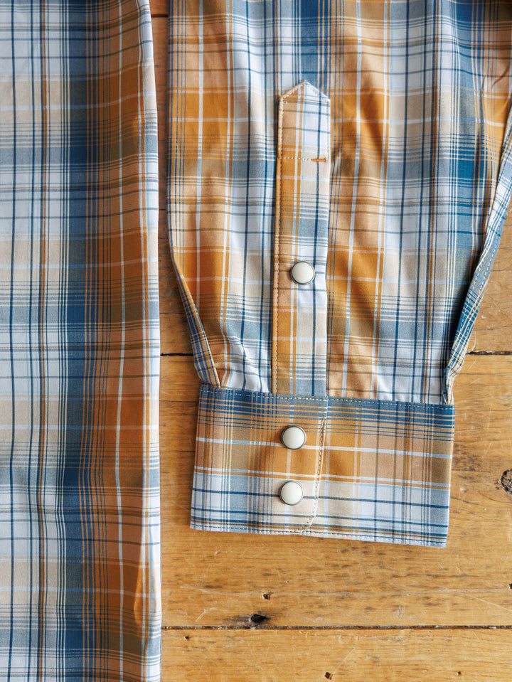 A close-up of a Stapleton Ariat Men's Plaid Pearl Snap shirt sleeve by Savannah Sevens western life{&}style shows three white snap buttons on the cuff, laid on a wooden surface.