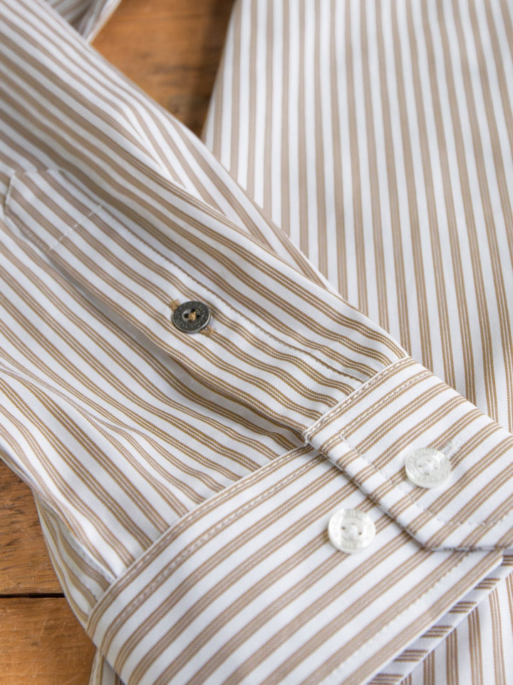A close-up of the Steger Cinch Men's White Pinstripe Button Up by Savannah Sevens western life{&}style shows brown and white stripes, the cuff with two white buttons, and part of the sleeve laid on a wooden surface.