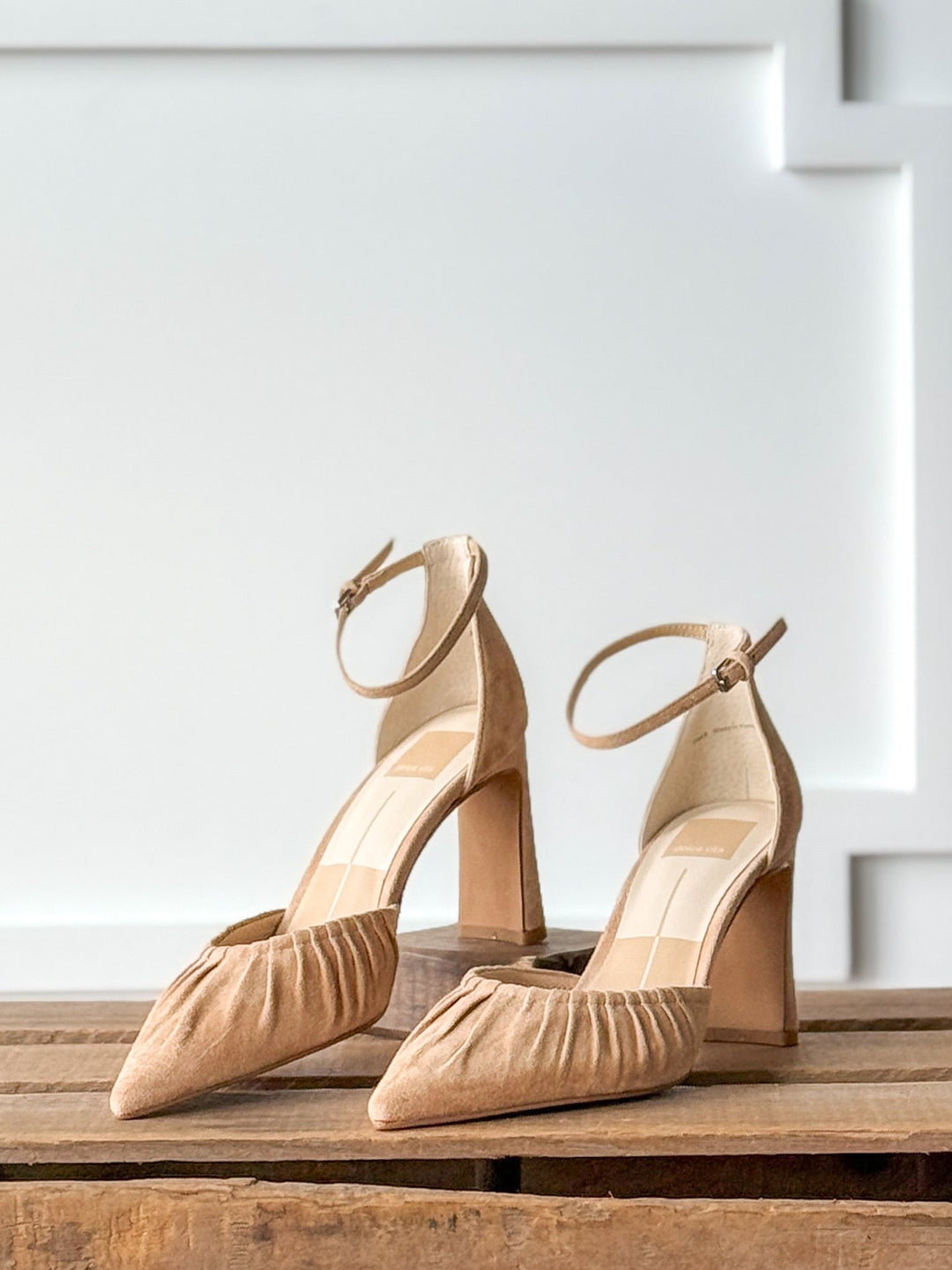 A pair of Savannah Sevens western life{&}style Stella Camel Suede Heel shoes featuring block heels, ruched pointed toes, and adjustable buckle ankle straps, displayed on a wooden surface against a white paneled background.