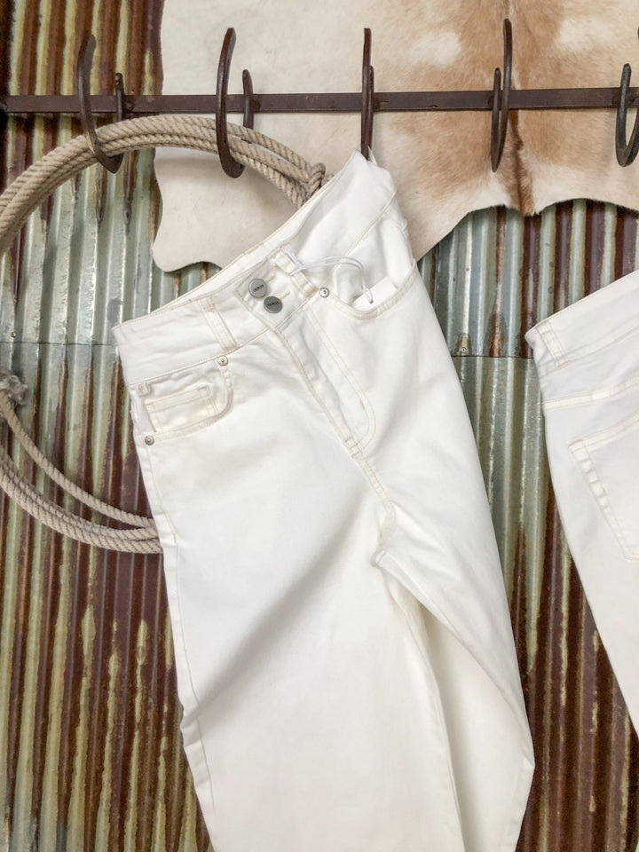 The Sterling High Rise Wide Leg Crop Jean by Savannah Sevens western life{&}style hangs on a rustic metal rod with coiled rope and cowhide accents, set against a corrugated metal wall.