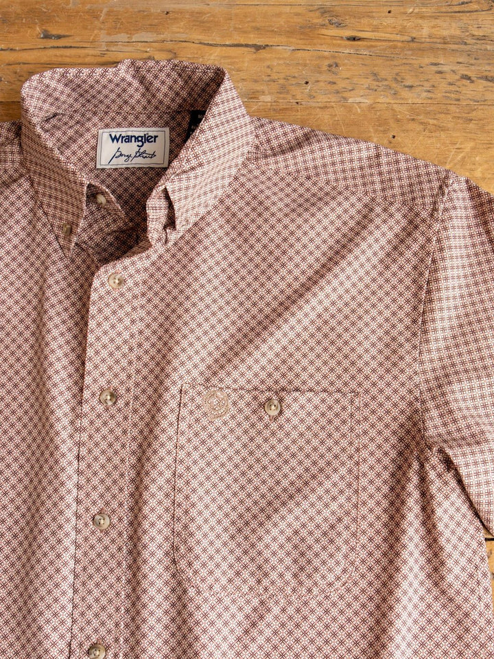 A beige and maroon patterned Strait Wrangler Men's Performance Button Up shirt from Savannah Sevens western life{&}style, featuring long sleeves, a front pocket, and button-up design, is laid flat on a wooden surface.