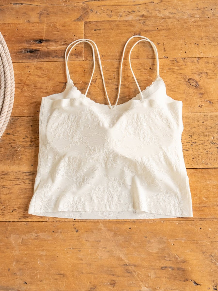 The Surrey Bralette by Savannah Sevens western life{&}style, featuring white lace and thin spaghetti straps, is displayed flat on a rustic wooden surface.
