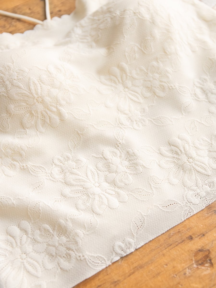 Close-up of the Surrey Bralette by Savannah Sevens western life{&}style, featuring delicate white lace fabric with floral patterns, displayed on a wooden surface.