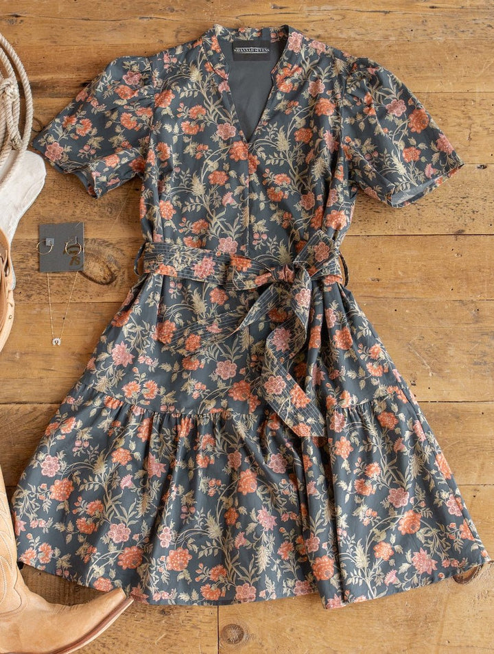 Sutherland Floral Puff Sleeve Dress by Savannah Sevens western life{&}style, styled with a belt, is laid flat on a wooden surface alongside tan cowboy boots and layered gold necklaces.