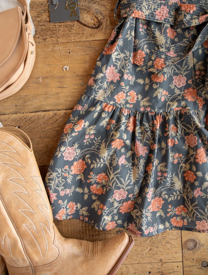 The Sutherland Floral Puff Sleeve Dress by Savannah Sevens western life{&}style, paired with tan cowboy boots, beige sandals, and a gold necklace, is displayed on a wooden surface.
