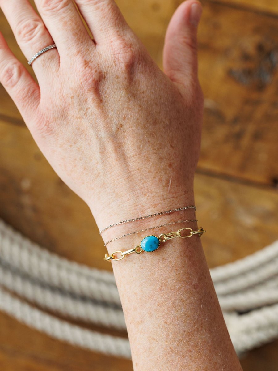 A hand wearing three Savannah Sevens western life{&}style bracelets, including the Suwanee Bracelet, rests on a wooden surface with thick rope in the background.