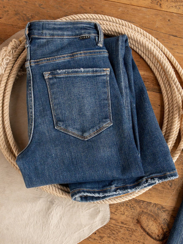 A pair of folded Tagan High Rise Relaxed Straight Leg Jeans by Savannah Sevens western life{&}style rests on a coiled rope atop wood, with part of a white cowhide visible nearby.